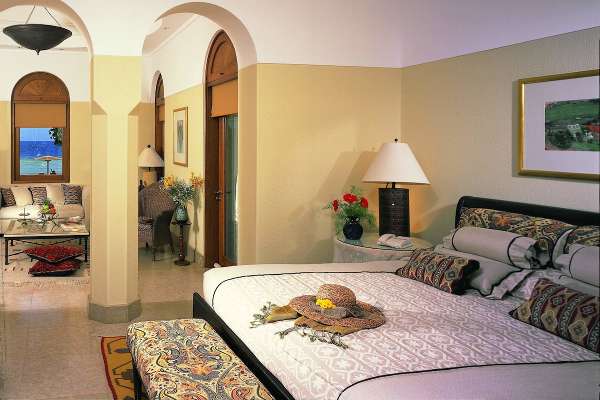 A hotel room with a bed, a sofa, a desk, and a view of the ocean through a window.
