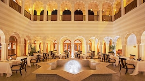 A spacious hotel lobby with multiple dining areas, a central fountain, and a mezzanine level with balconies. - The Oberoi, Sahl Hasheesh (Hurghada)