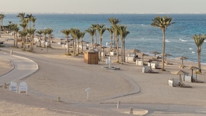 A beach with palm trees, beach umbrellas, and a wooden structure. - The Oberoi, Sahl Hasheesh (Hurghada)