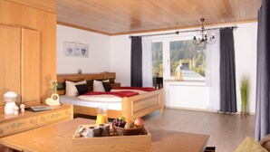 Une chambre à coucher avec un lit en bois, une table de chevet sur laquelle se trouve un panier de fruits, une fenêtre donnant sur des arbres et un lustre.