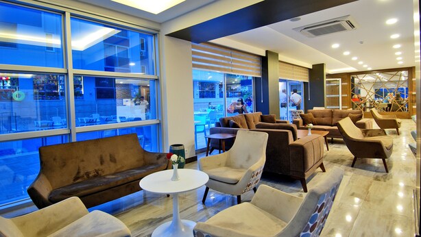 A modern lounge area with comfortable seating, large windows, and a view of the street outside. - Kleopatra Ramira Hotel - All Inclusive (Alanya)