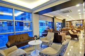 A modern lounge area with comfortable seating, large windows, and a view of the street outside. - Kleopatra Ramira Hotel - All Inclusive (Alanya)