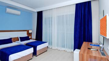 A hotel room with two beds, a desk, a computer, and a large window with curtains.