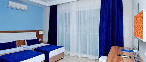 A hotel room with two beds, a desk, a computer, and a large window with curtains.