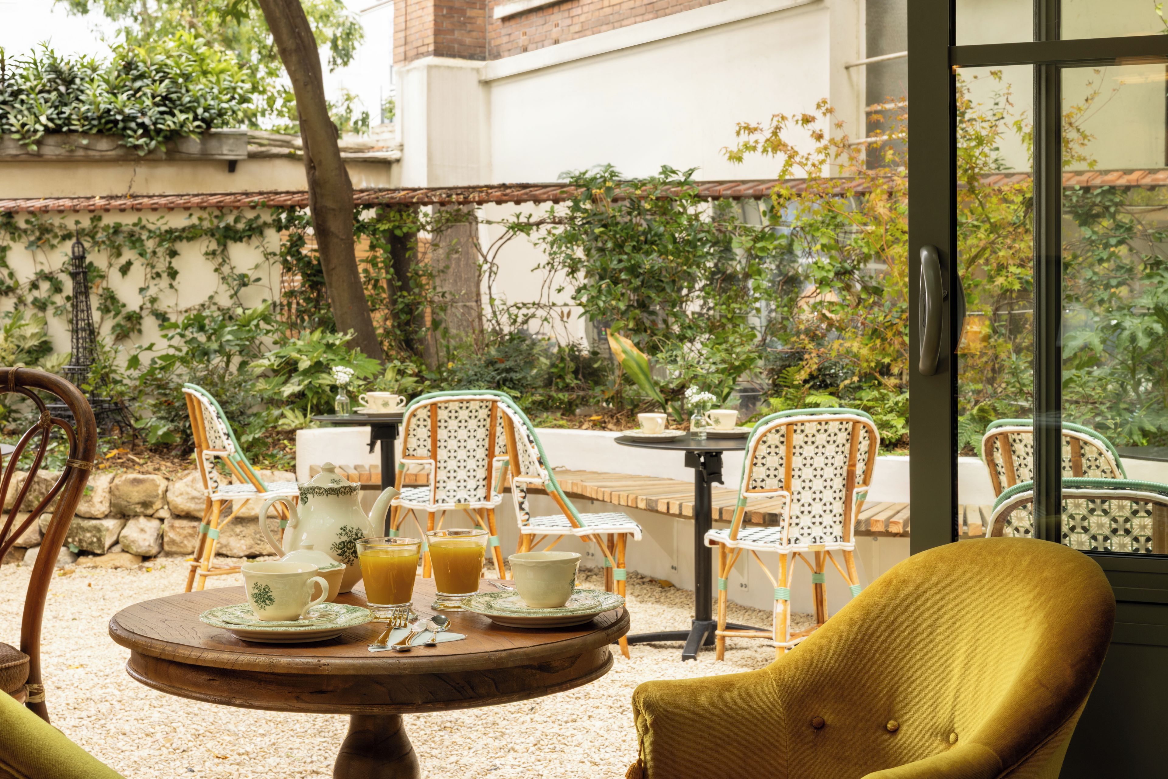 Un espace extérieur aménagé avec des chaises en osier, une table ronde en bois et un verre de jus d’orange.