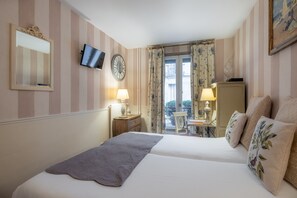 A hotel room with a large bed, a television, a clock, and a balcony with a table and chair. - Hotel de l'Avre (Paris)