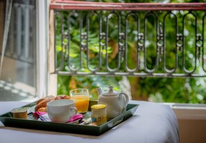 A breakfast tray with croissants, a cup, a glass of orange juice, a teapot, and a jar of jam on a table by a window with a metal railing. - Hotel de l'Avre (Paris)