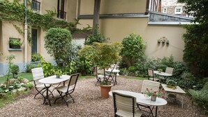 An outdoor patio with tables and chairs, surrounded by potted plants and a gravel ground. - Hotel de l'Avre (Paris)