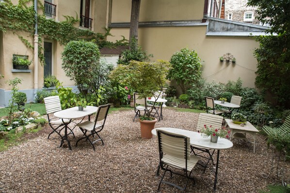 An outdoor patio with tables and chairs, surrounded by potted plants and a gravel ground. - Hotel de l'Avre (Paris)