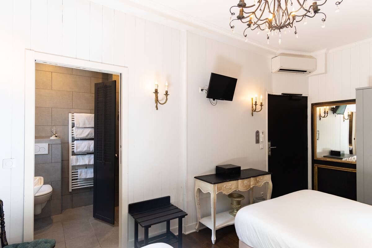 A hotel room with a bed, a desk, a television, and a bathroom visible through an open door.