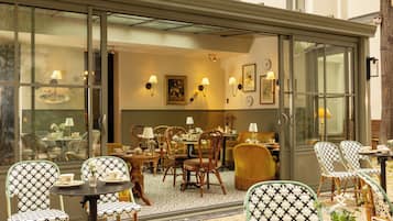 Un espace de restauration intérieur comprenant plusieurs tables et chaises, une cloison en verre et des luminaires fixés au mur.