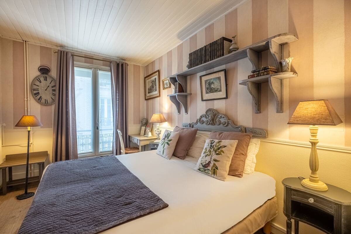 A hotel room with a large bed, striped wallpaper, a clock, and a balcony.