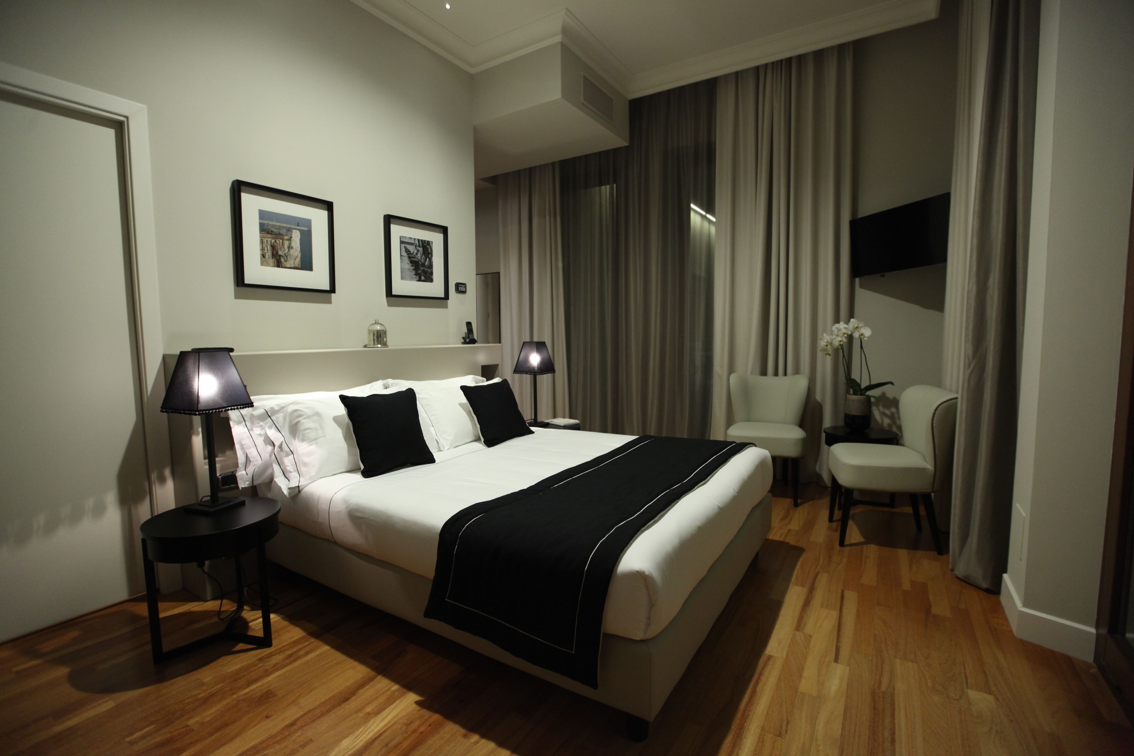 A neatly arranged hotel room with a large bed, two bedside tables with lamps, a chair, and a TV mounted on the wall.