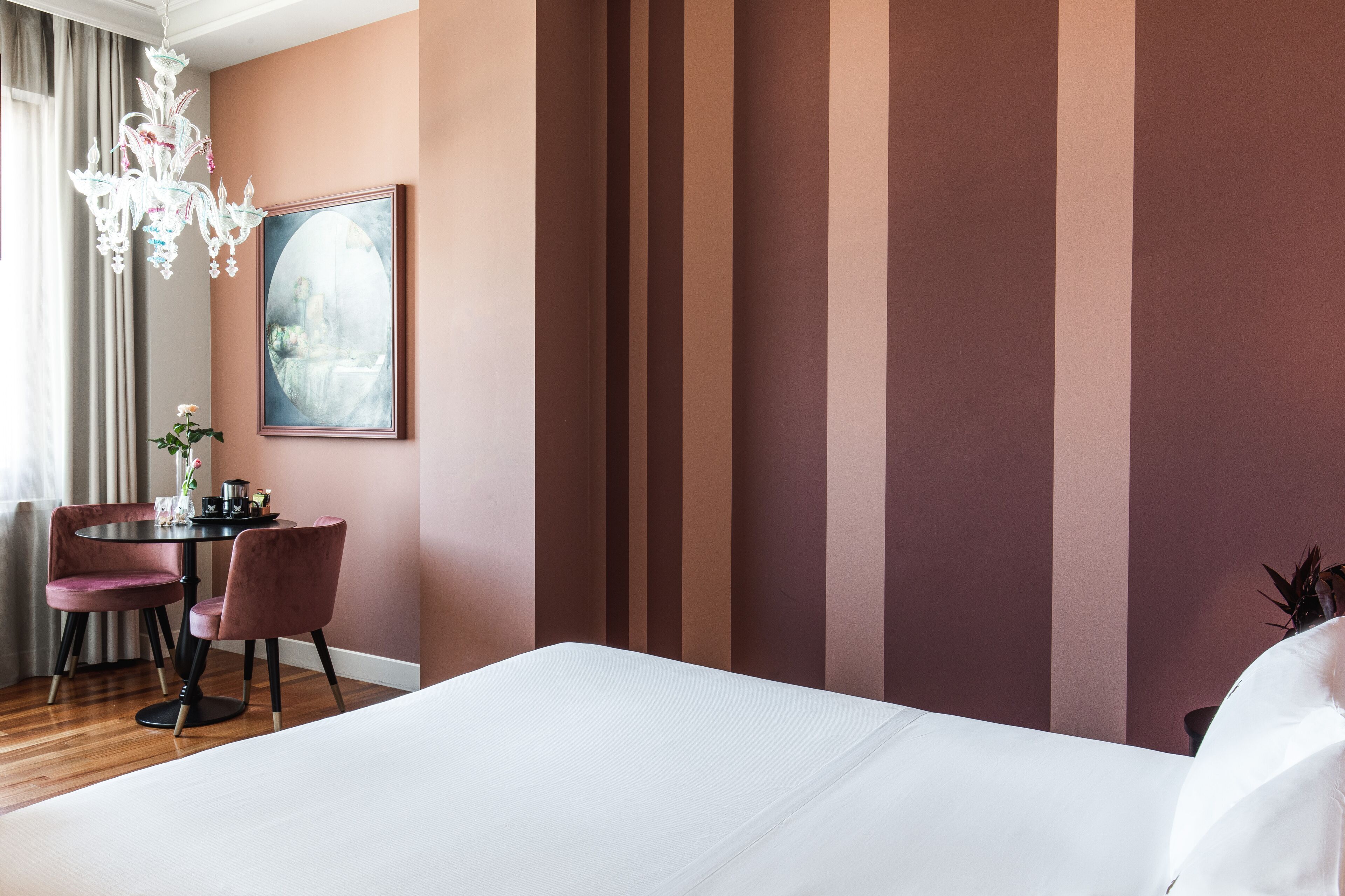 Una habitación de hotel con una cama grande, una mesa redonda con dos sillas, un candelabro y un cuadro en la pared.