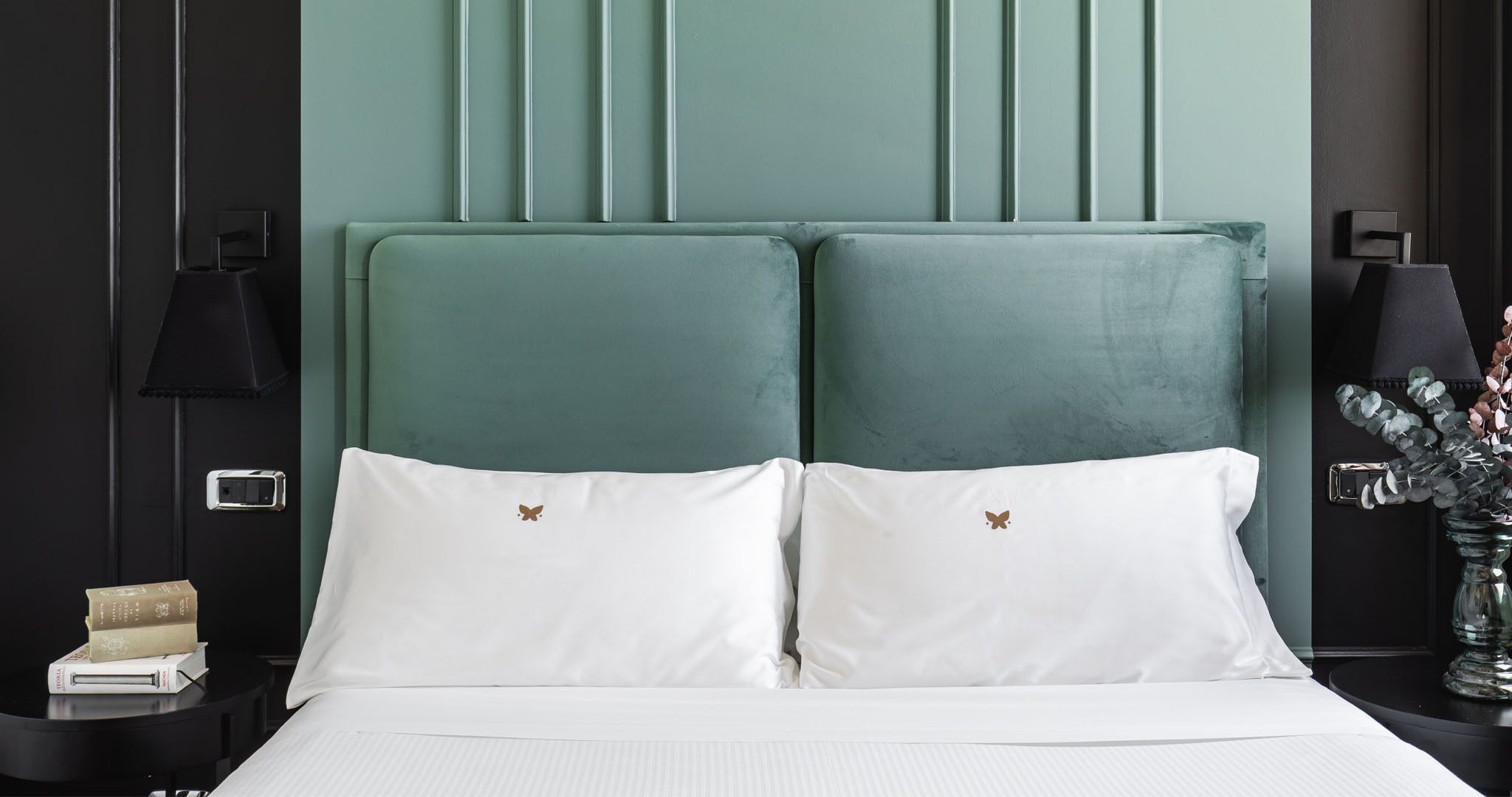 A bed with white bedding and two pillows, a bedside table with a lamp, and a wall with vertical paneling.