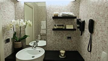 A bathroom with a white sink, a mirror, a potted orchid, a black countertop, a towel, a phone, and toiletries on a shelf.