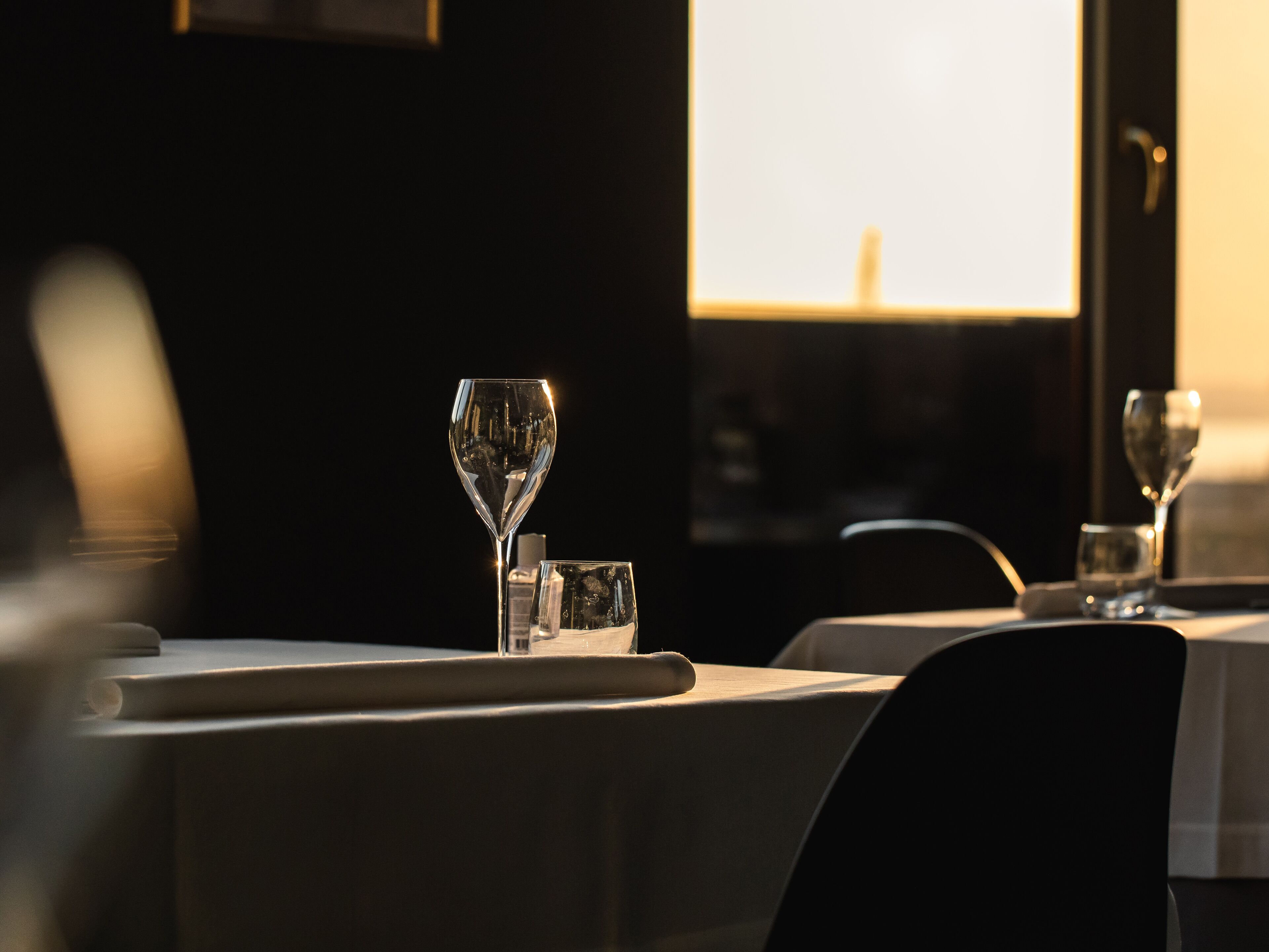 Un ambiente de restaurante con una mesa dispuesta para dos personas, que incluye una copa de vino y un vaso de agua.