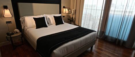 Habitación de hotel con una cama grande, una mesita de noche con lámpara y vistas al exterior por la ventana.