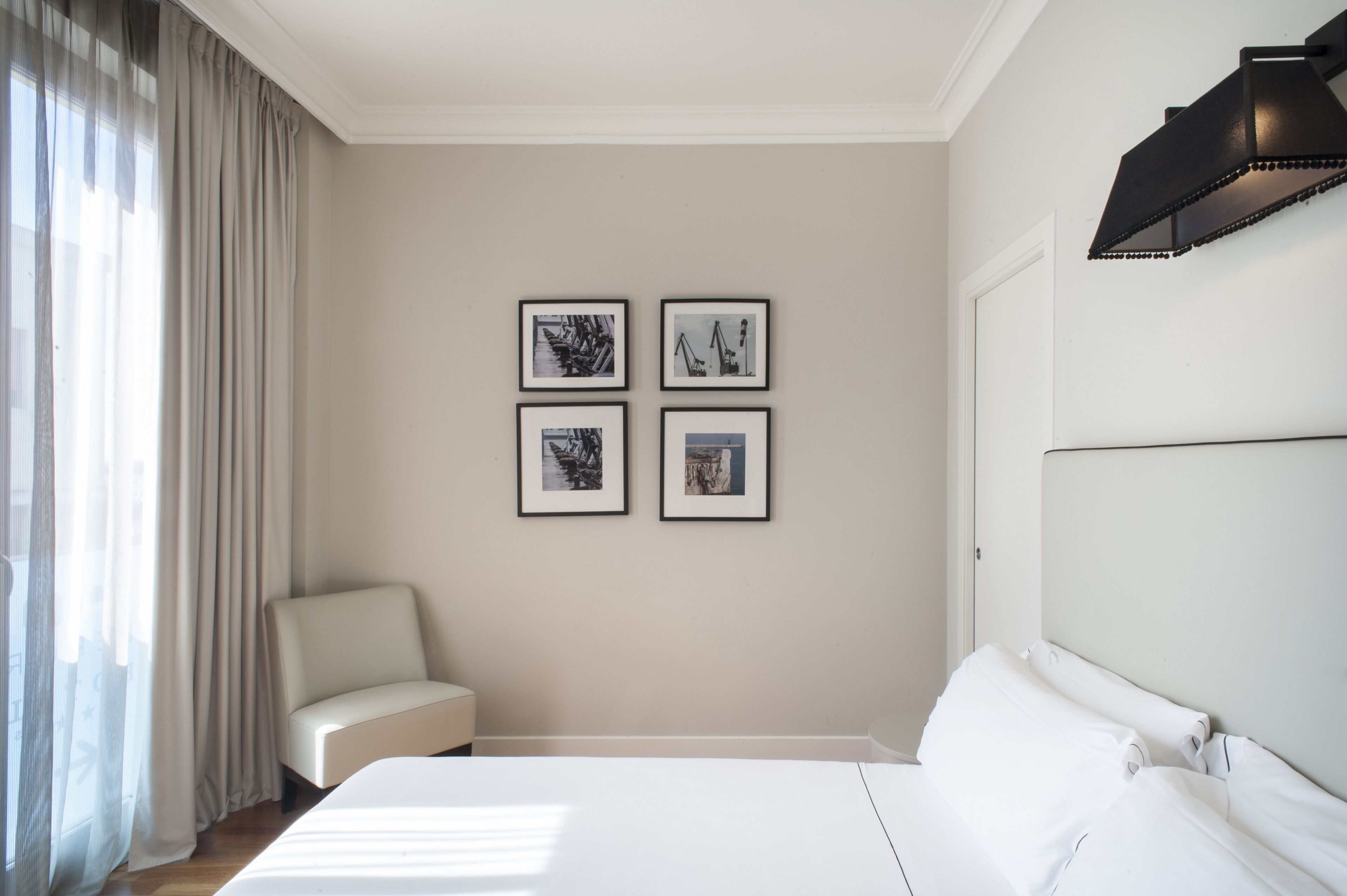 Una habitación de hotel con una cama, una silla y cuatro cuadros en la pared.