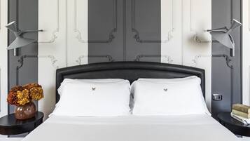 A neatly made bed with white linens and two pillows, flanked by two bedside tables with lamps, a vase of flowers, and a stack of books on one table.