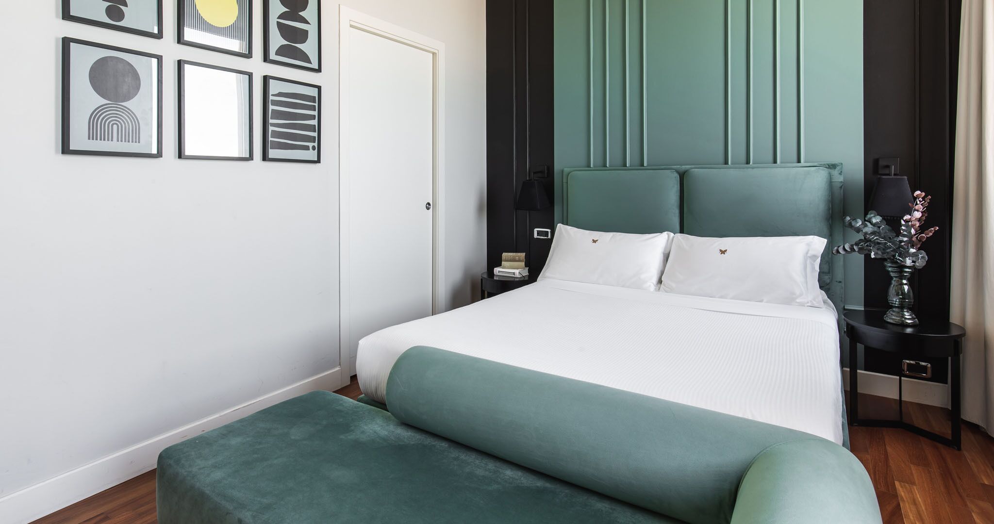 A neatly arranged hotel room with a large bed, a bedside table with a lamp, and a small nightstand.