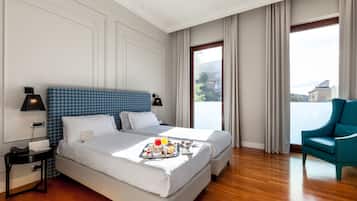 Una habitación de hotel con dos camas, una mesa de comedor con desayuno, una silla y un ventanal con cortinas.