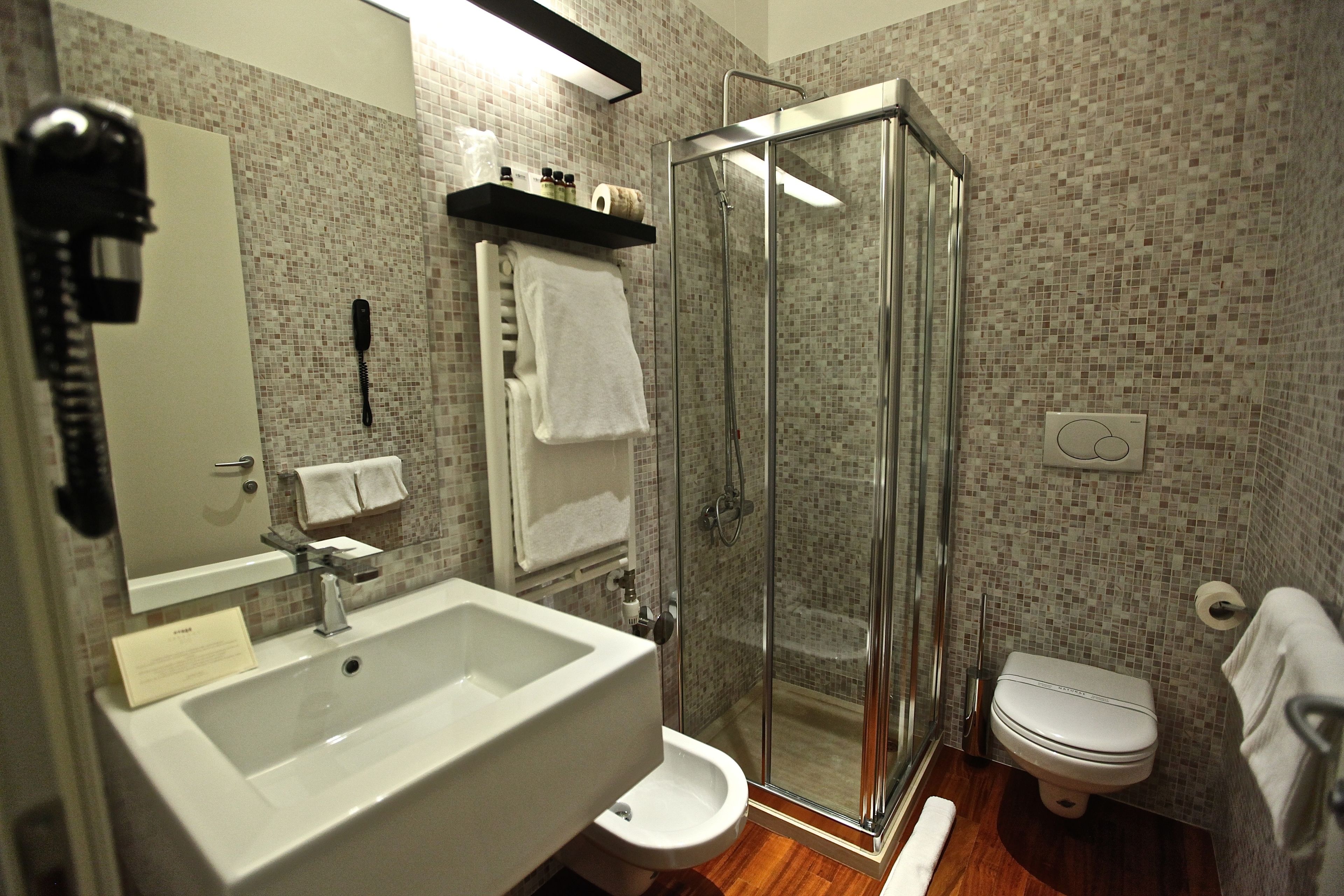A bathroom with a glass shower enclosure, a sink, a toilet, and a mirror.