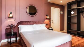 A bedroom with a large bed, a round mirror, two wall sconces, a small side table with a vase, and a wardrobe with hanging shoes.