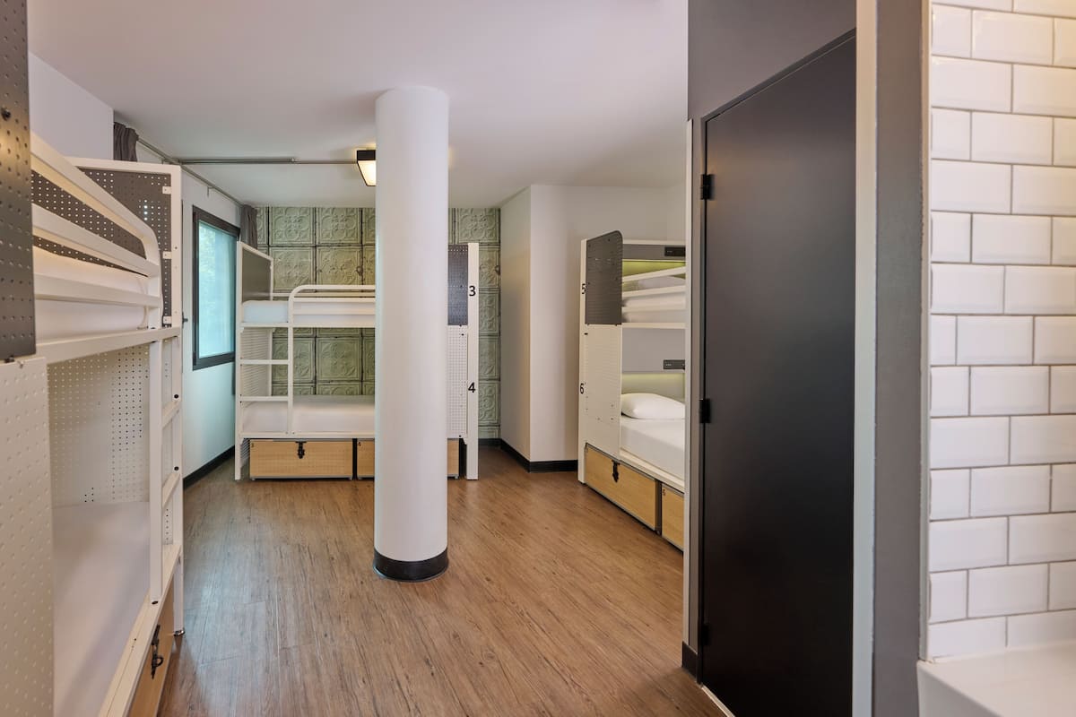 Habitación de hotel con literas, suelo de madera y pared de azulejos.