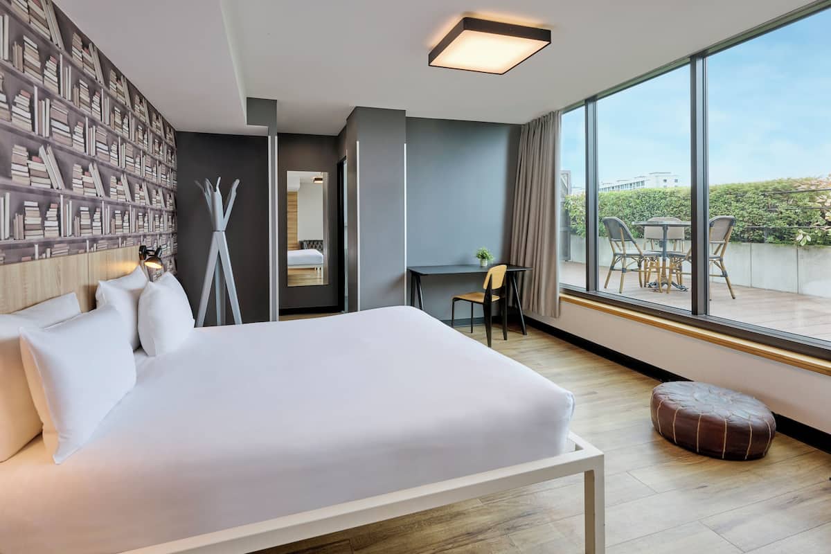 Una habitación de hotel moderna con una cama grande, un escritorio y un balcón con sillas.