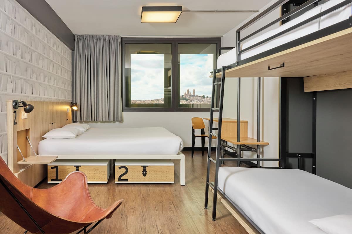 Una habitación de hotel moderna con literas, un escritorio, una silla y un amplio ventanal con vistas a la ciudad.