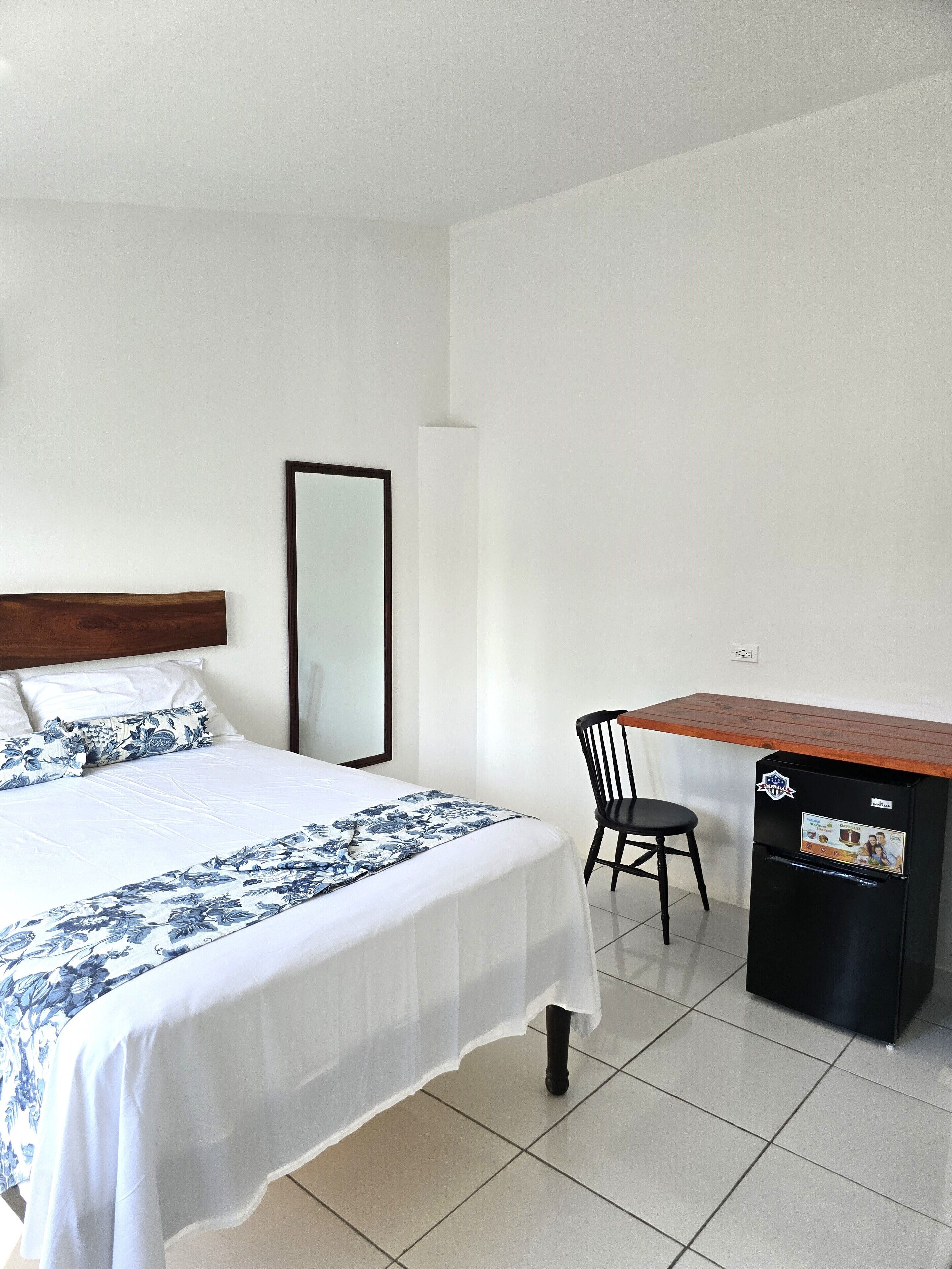 Una camera d'albergo con un letto, una sedia, una scrivania e un frigorifero.
