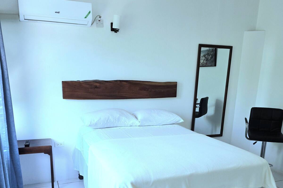 A clean, modern hotel room with a bed, bedside table, and a large mirror.