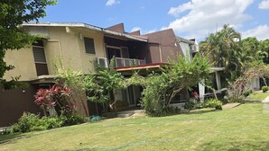 Un edificio residencial de dos pisos, con balcón y un césped bien cuidado con zona de jardín.