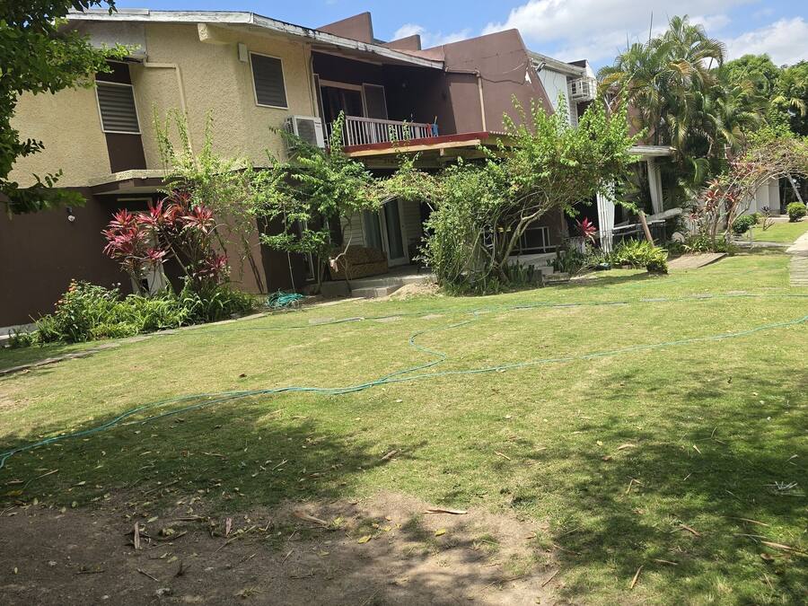 A residential building with a two-story structure, a balcony, and a well-maintained lawn with a garden area.