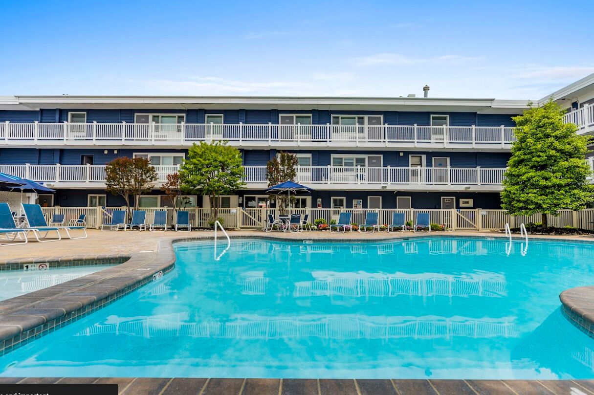 A swimming pool with lounge chairs and umbrellas, surrounded by a building with balconies.