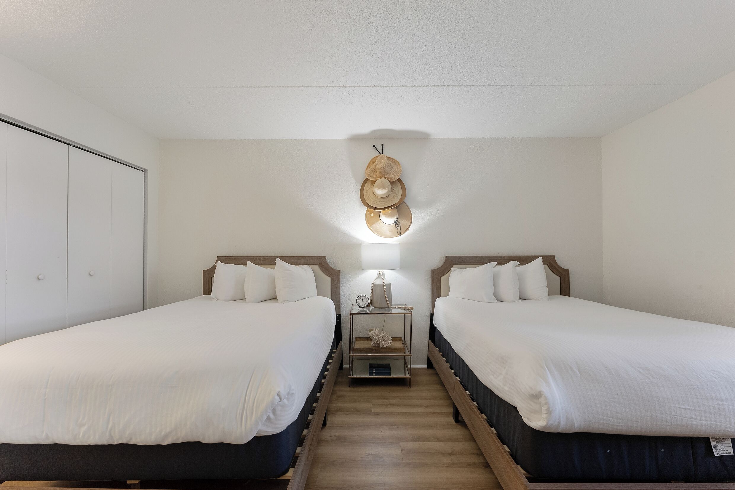 Habitación doble con dos camas, una mesita de noche con lámpara y un perchero en la pared.
