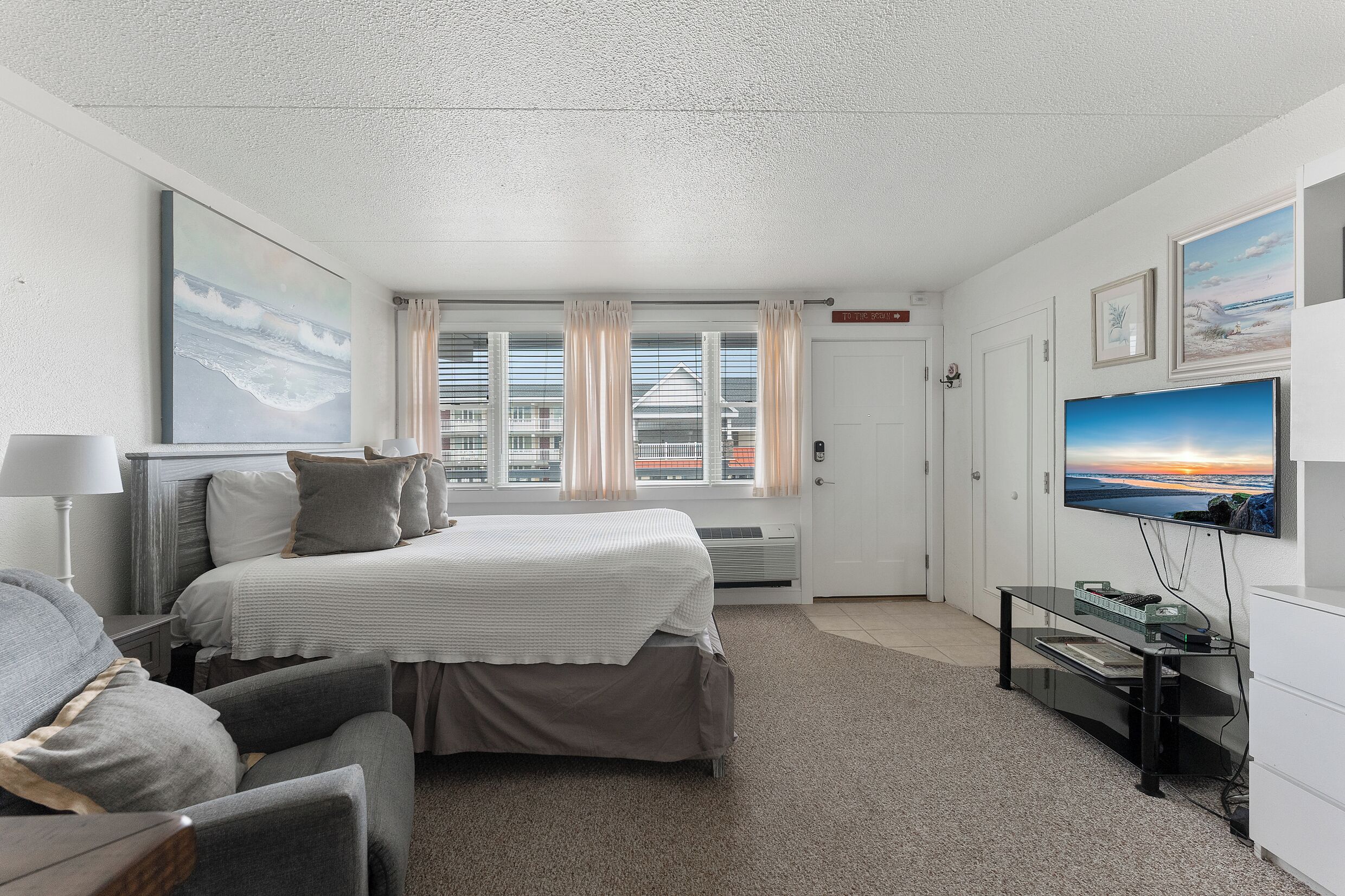 A hotel room with a bed, a desk with a computer, a TV, and a window with curtains.