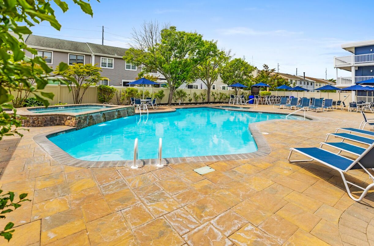 A swimming pool with lounge chairs and umbrellas, surrounded by a stone patio.
