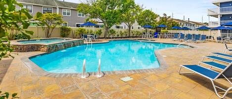 A swimming pool with lounge chairs and umbrellas, surrounded by a stone patio.
