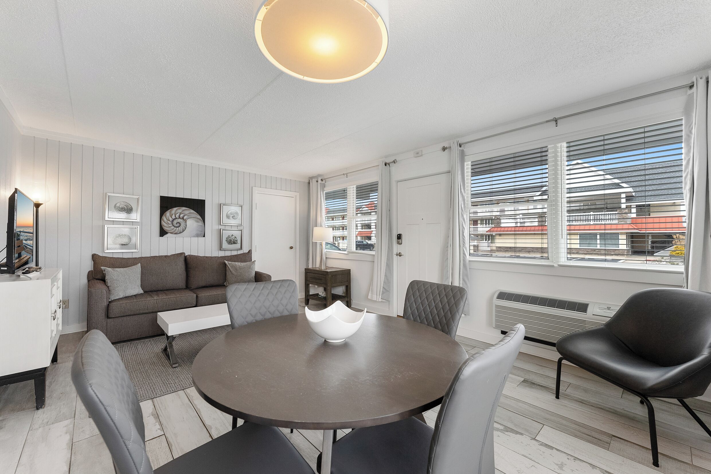 Ein modernes Wohnzimmer mit einem runden Esstisch, grauen Polsterstühlen, einem grauen Sofa und einem weißen Beistelltisch.