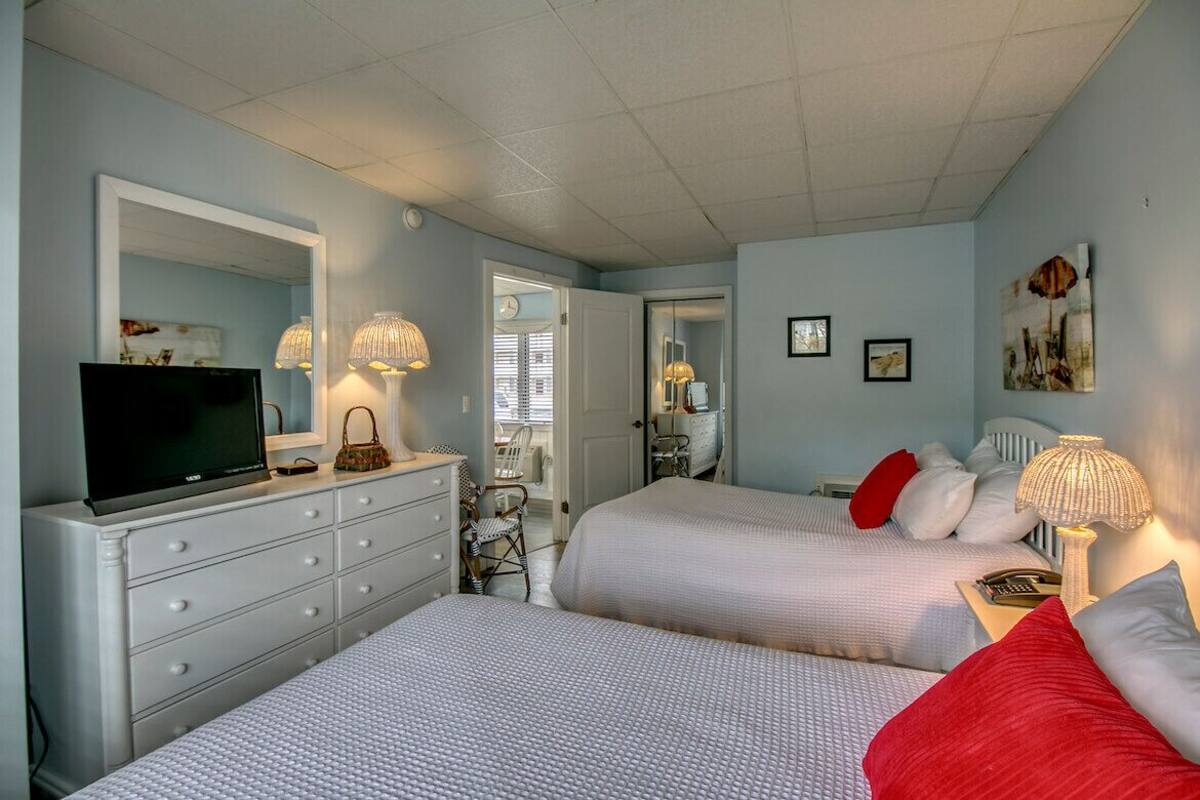 A bedroom with two beds, a dresser, a television, and a mirror.