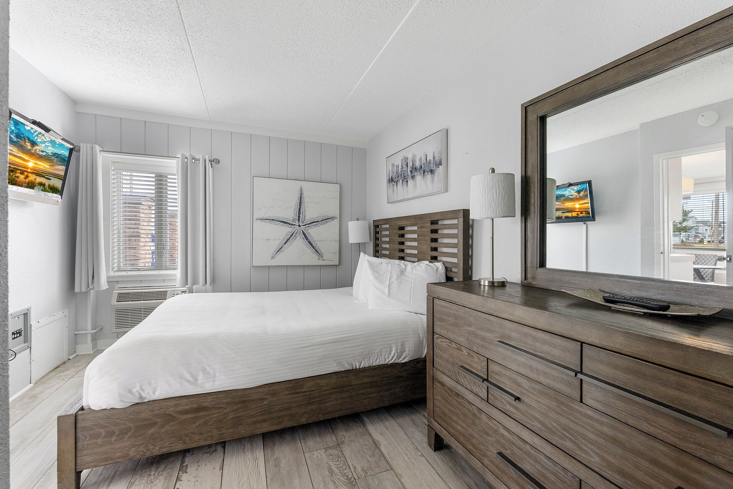 A bedroom with a wooden bed, a dresser, a mirror, and artwork on the walls.