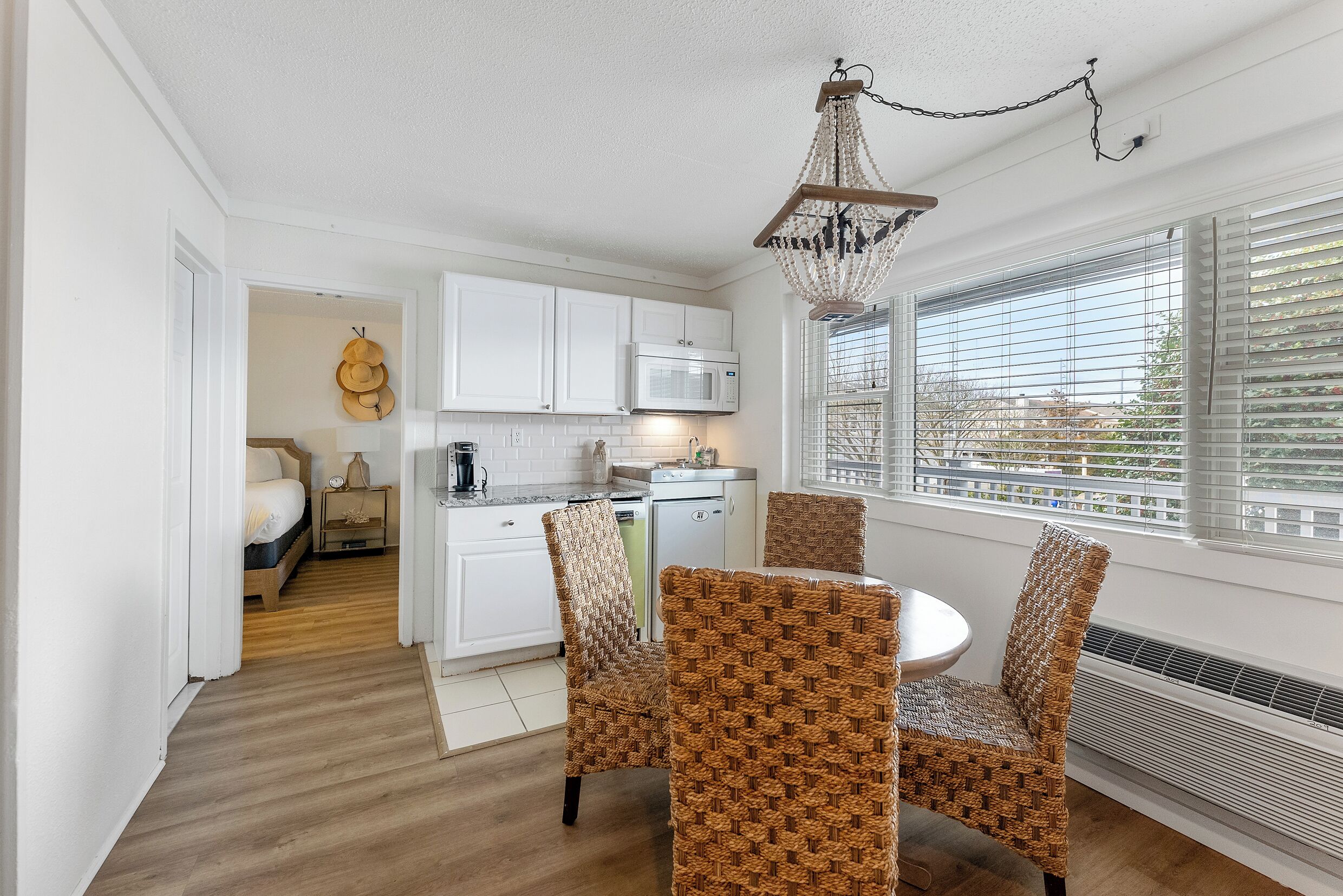 A compact kitchen with white cabinets, a microwave, and a dining area with wicker chairs.
