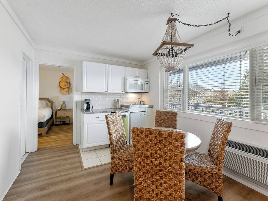 A compact kitchen with white cabinets, a microwave, and a dining area with wicker chairs.