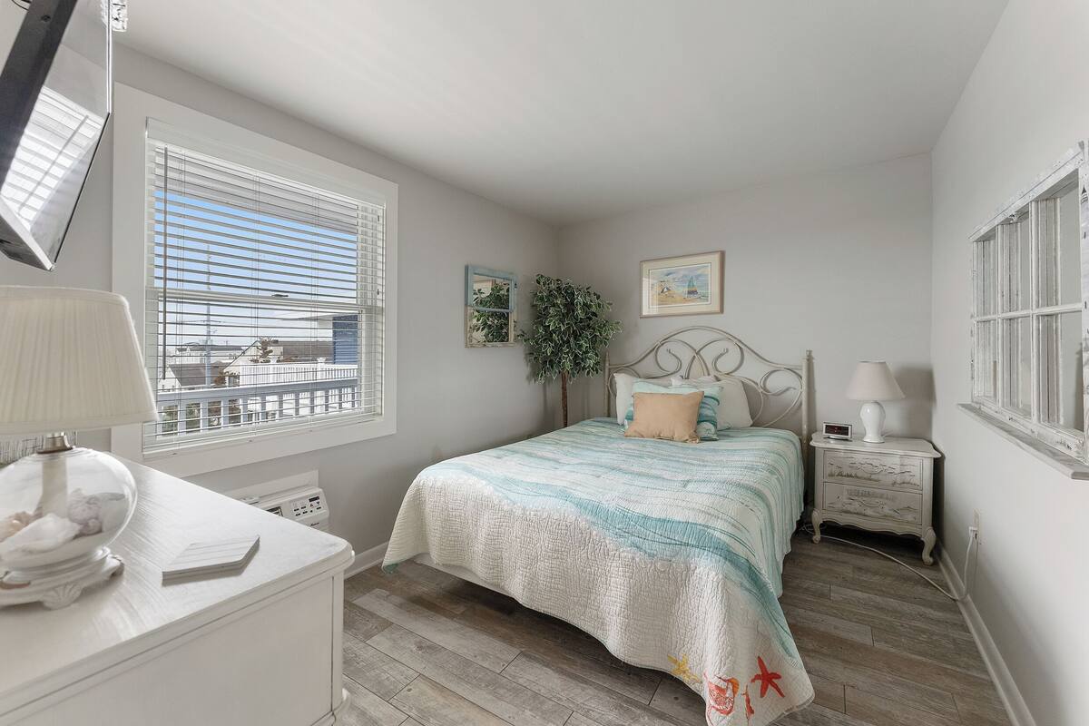 A bedroom with a bed, bedside tables, a lamp, a plant, and a window.