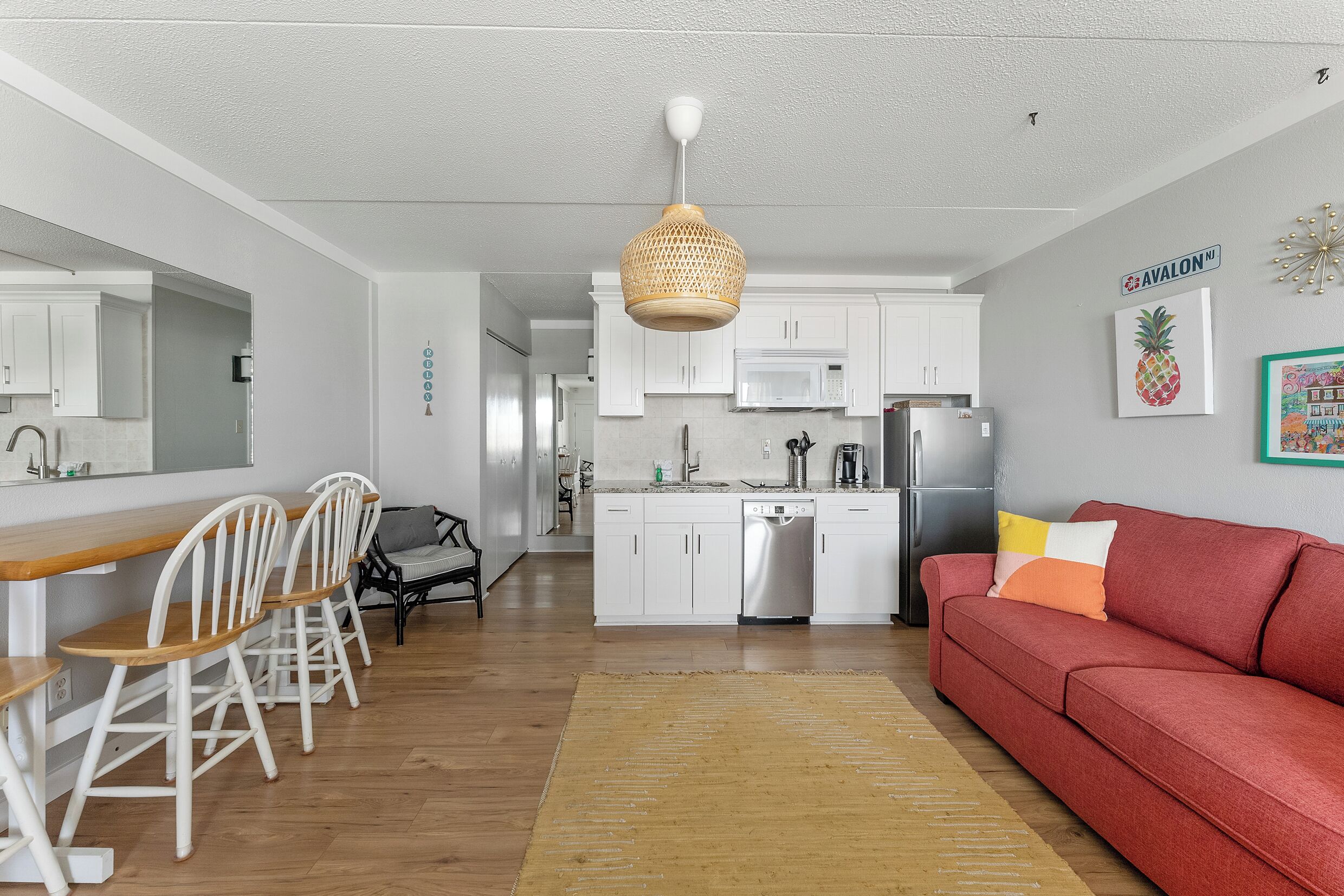 A modern kitchen with white cabinets, a wooden dining table, and a red sofa.