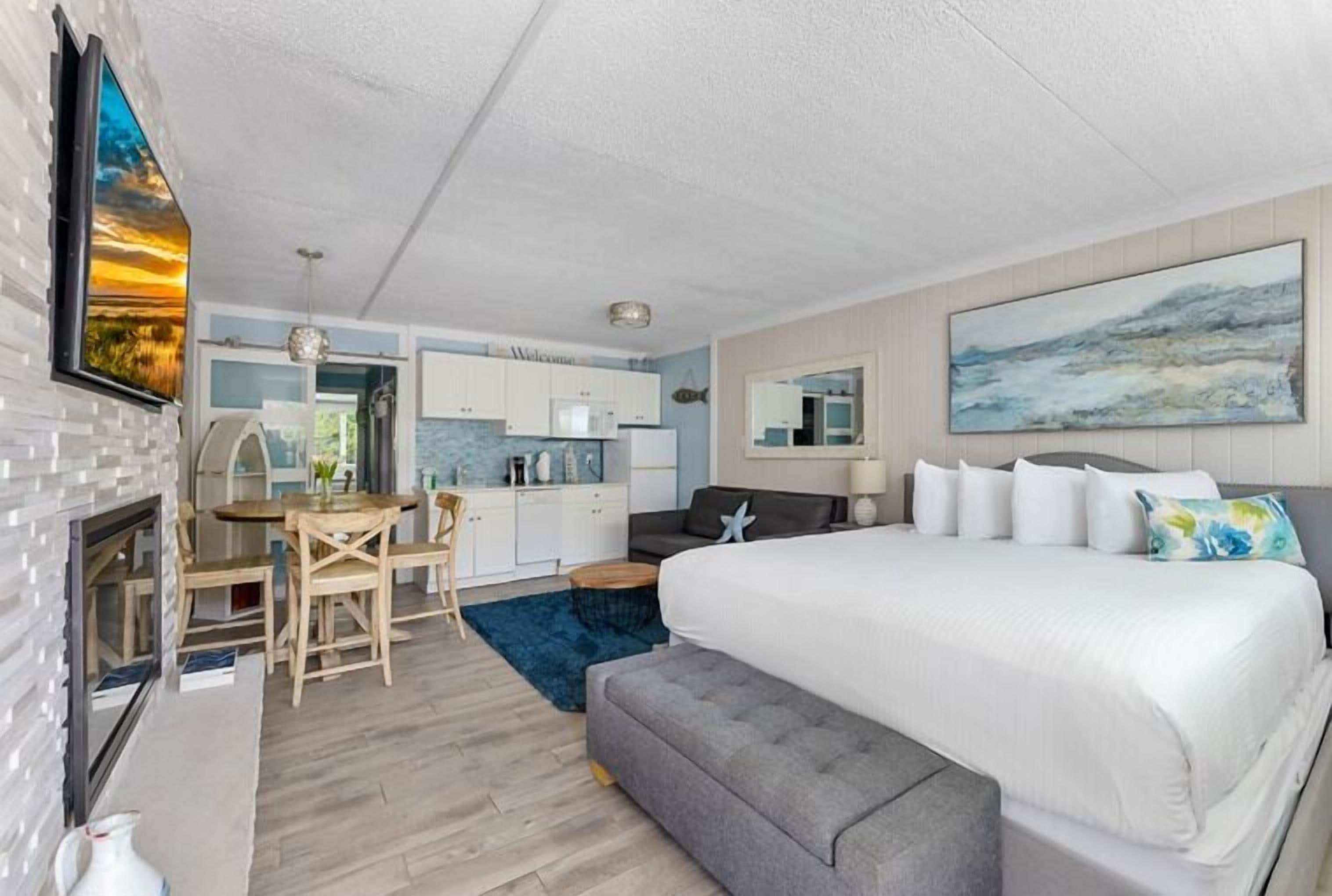 A modern hotel room with a large bed, a dining area, and a kitchen.