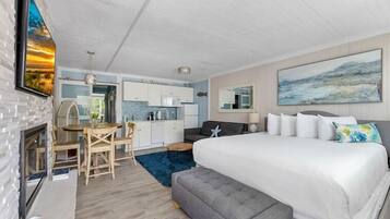 A modern hotel room with a large bed, a dining area, and a kitchen.
