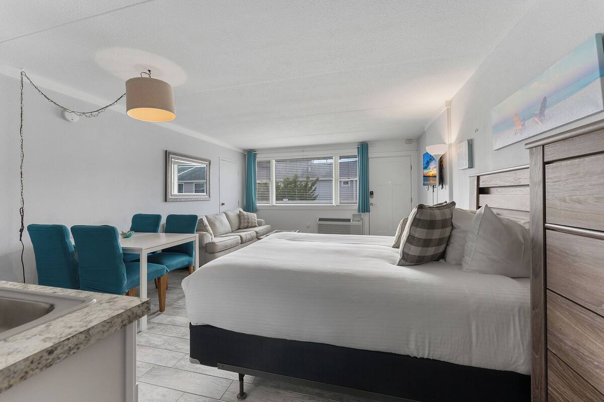 A modern bedroom with a large bed, a dining table, and a kitchenette.